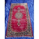 A hand woven Oriental red ground worn wool carpet, with a decorative floral medallion and frieze,