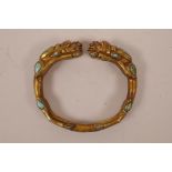 A Chinese gilt metal bangle with twin dragon head decoration and set with turquoise stones, 3"