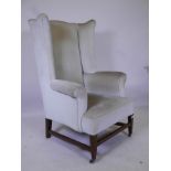 A C19th Georgian style wing backed armchair, raised on tapering supports united by stretchers