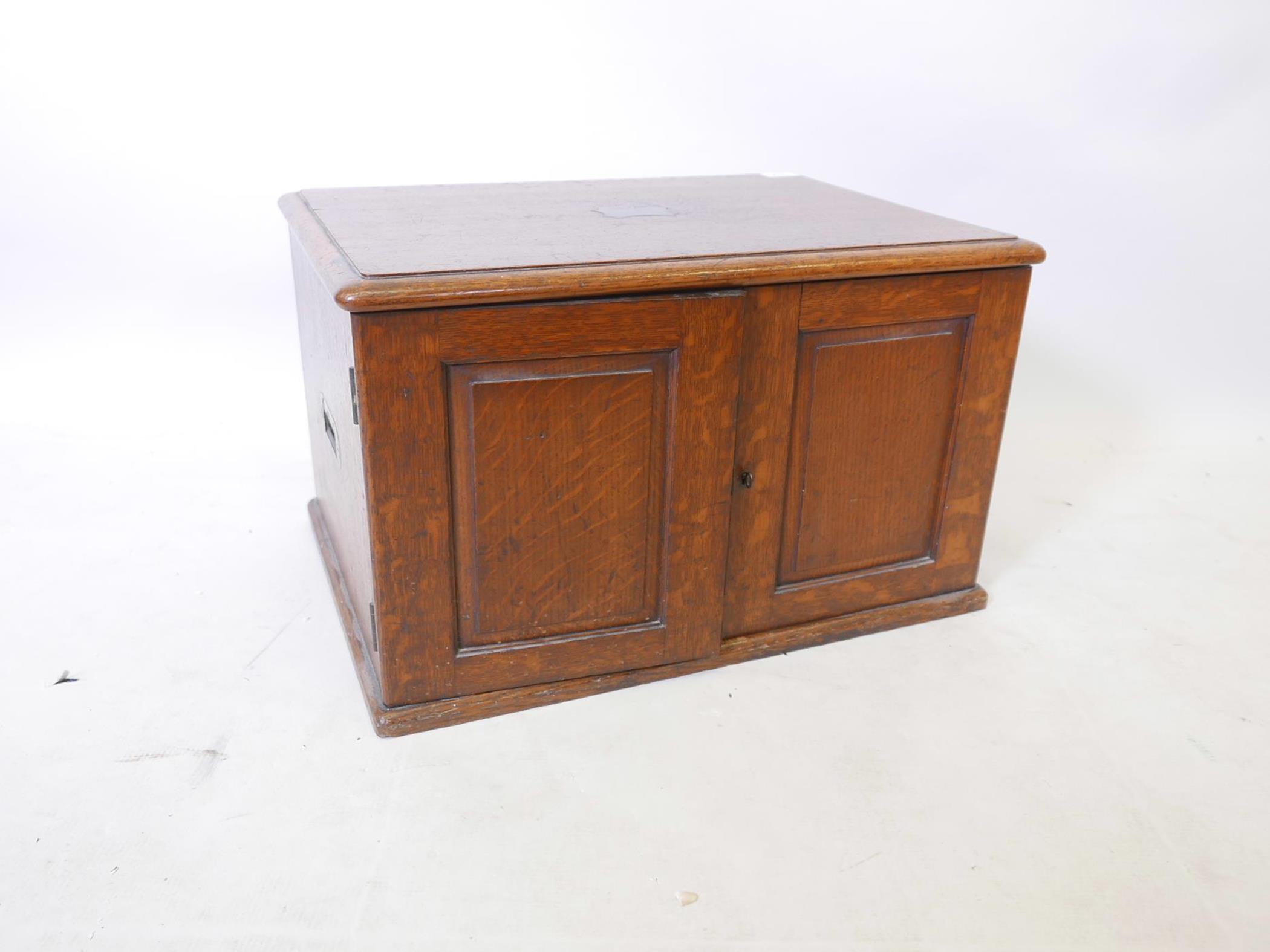 An Edwardian oak cutlery canteen with two panelled doors and brass carrying handles, concealing four