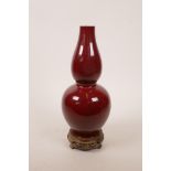 A Chinese sang de boeuf glazed porcelain double gourd vase on a carved hardwood stand, four