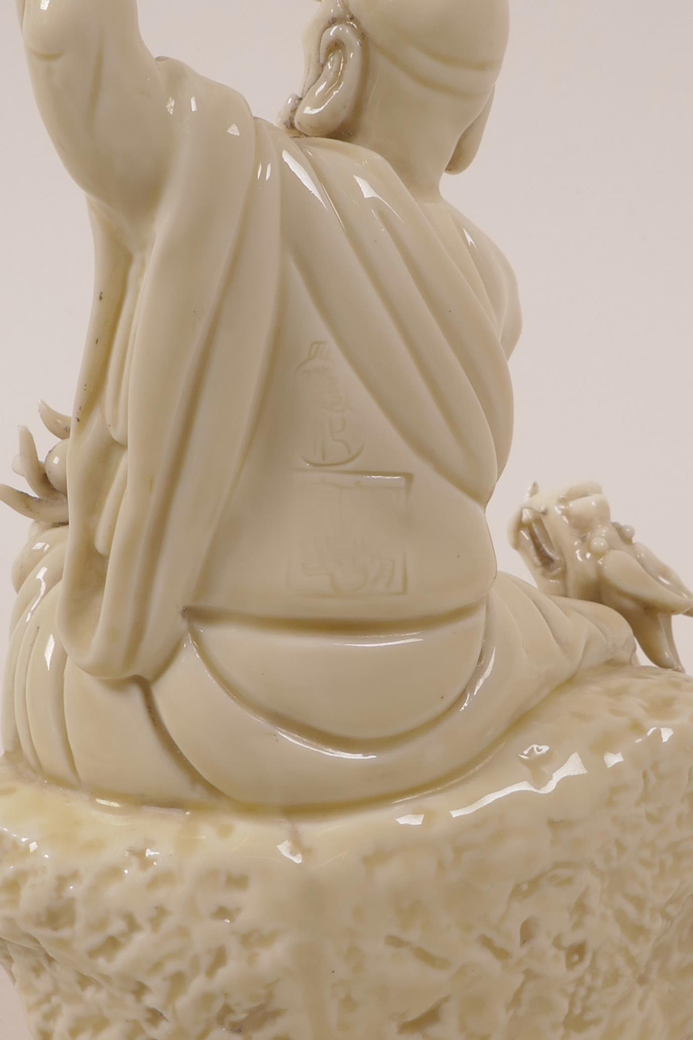 A Chinese blanc de chine porcelain Lohan seated on a rock with a dragon, impressed marks, A/F - Image 3 of 4