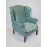 A green leather wing armchair with studded decoration and reeded supports