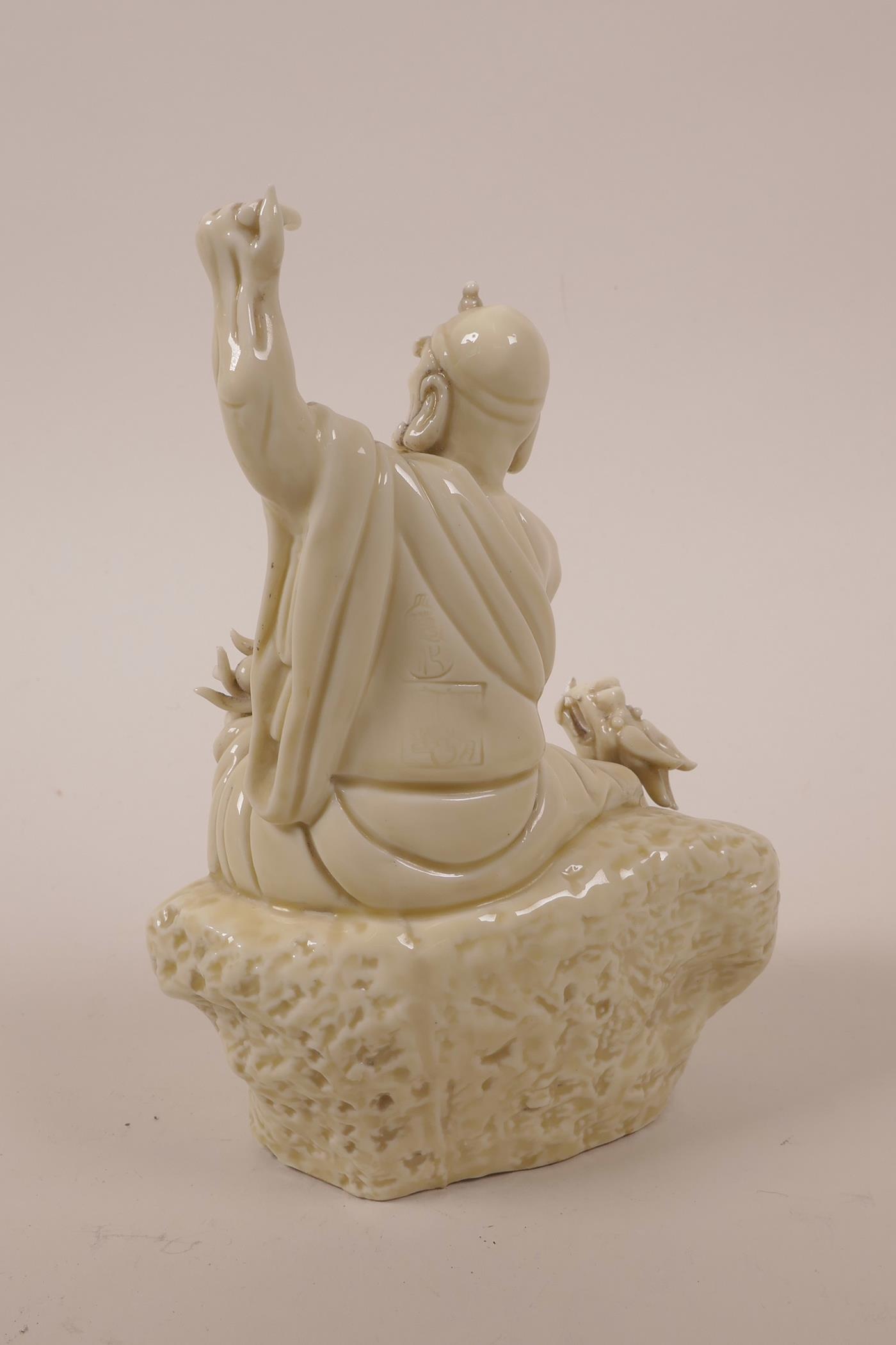 A Chinese blanc de chine porcelain Lohan seated on a rock with a dragon, impressed marks, A/F - Image 2 of 4