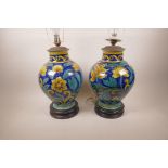 A good pair of Majolica table lamps painted with flowers and leaves, on turned wood bases, 17" high