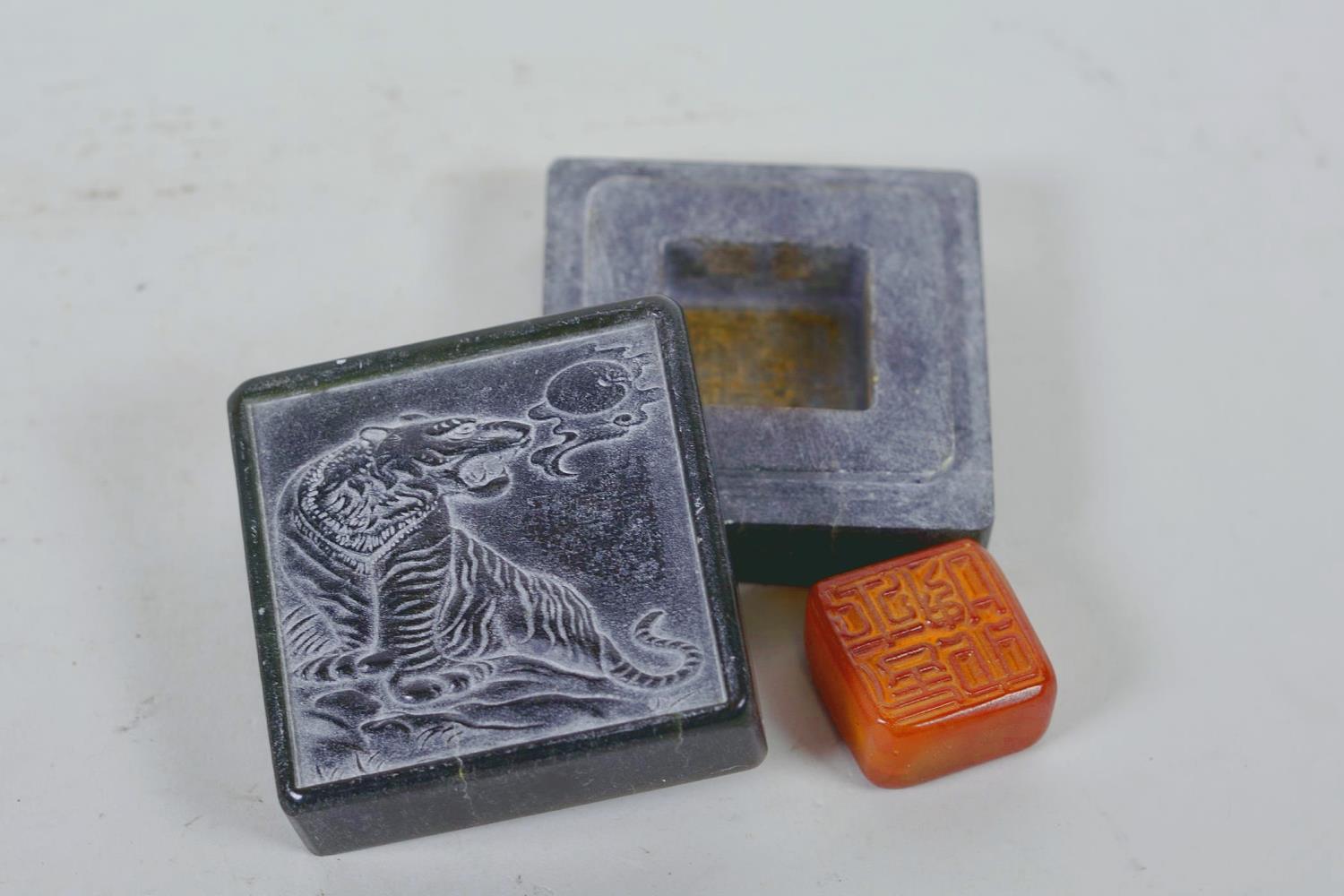 A Chinese green soapstone box containing an amber stone seal, the cover carved with a tiger, 6