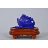 A Chinese carved lapis ornament in the form of a kylin atop a money token, on a wood stand, 6"