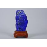 A Chinese carved lapis ornament in the form of a mountain landscape, on a wood stand, 7" high