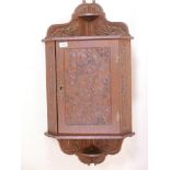 An Arts and Crafts oak hanging corner cupboard, with carved decoration of trailing brambles, 18" x