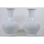 A pair of Chinese porcelain vases with flared necks, all over cream/blue glaze and carved scroll and