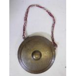 An Indonesian bronze temple gong, with intricate incised decoration, and a hand woven strap, 10"