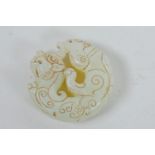 A Chinese light green hardstone pendant with carved mythical creature decoration, 2" diameter