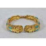 A Chinese gilt metal bangle with twin dragon heads to end, set with turquoise and coral stones,