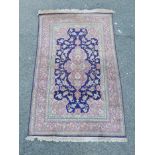 A Persian rug with a pink floral medallion design on a blue field, worn, 50" x 77"
