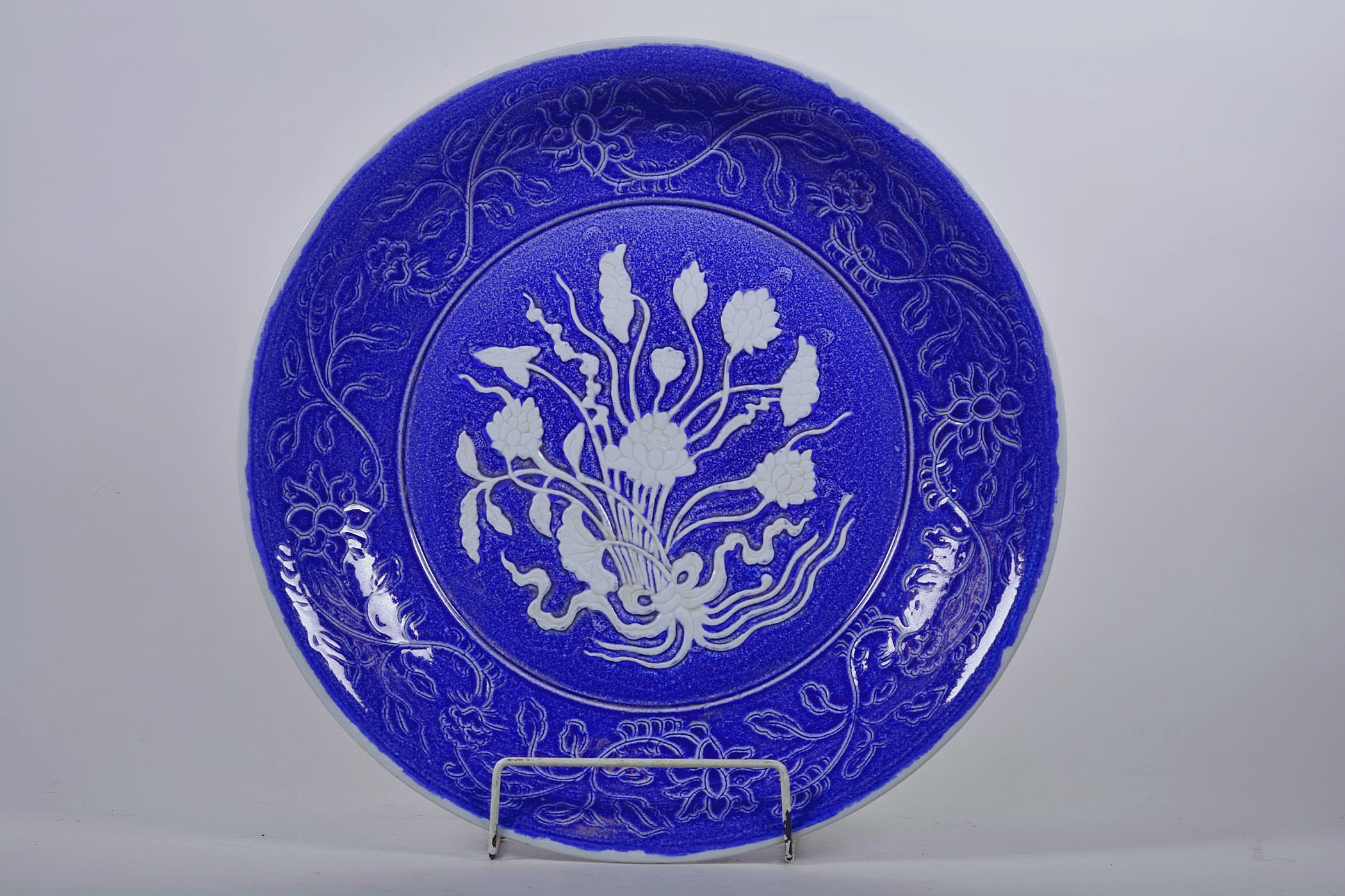 A large Chinese blue and white pottery charger with raised and incised floral decoration, incised