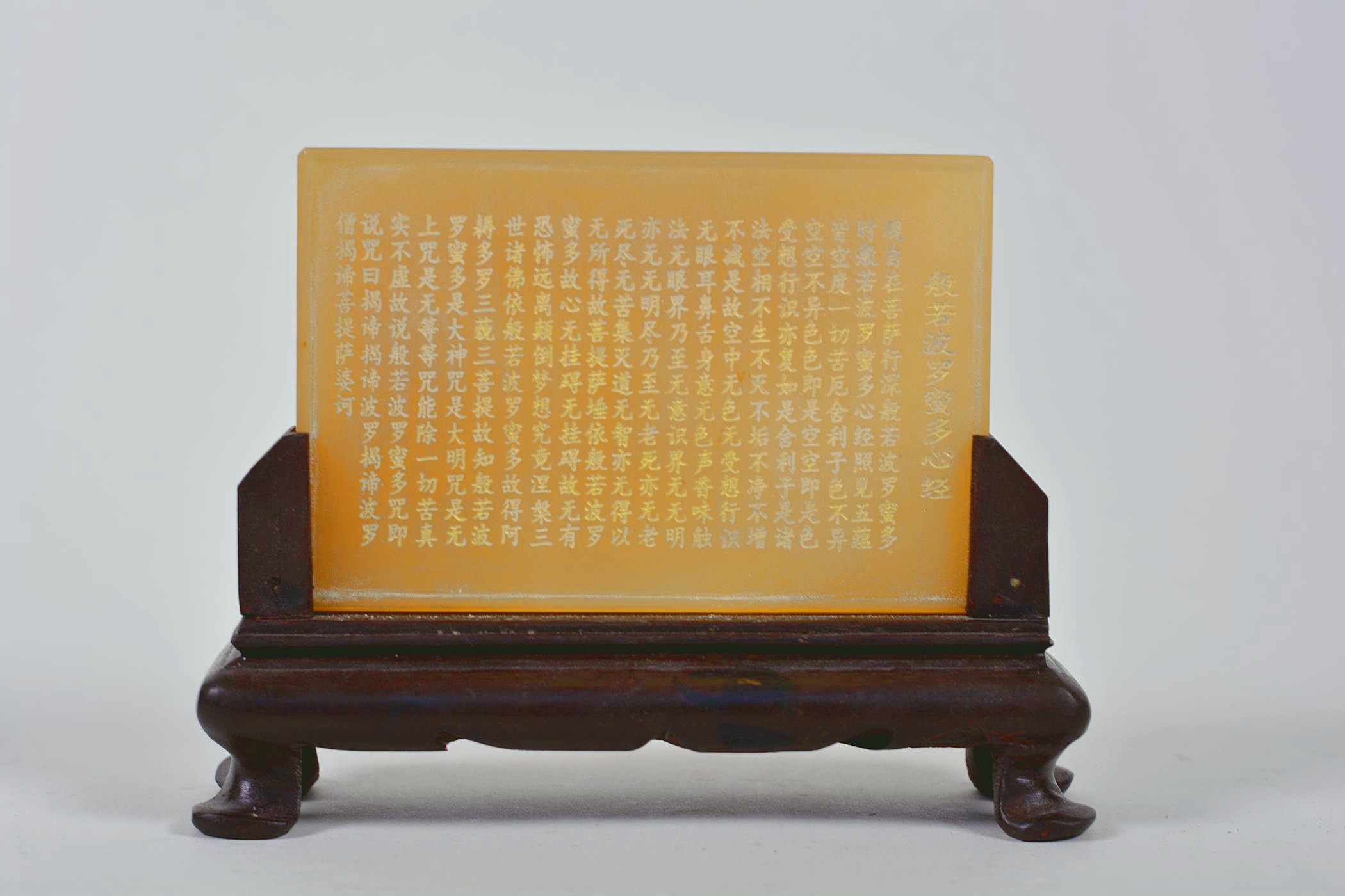 A Chinese amber soapstone tablet with character inscription decoration, mounted on a carved hardwood