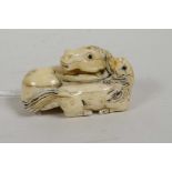 A Japanese bone netsuke carved in the form of a mare and foal, with glass eyes, signed, 2" long