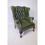 A Georgian style wing back armchair, with buttoned leather and brass studs, raised on ball and