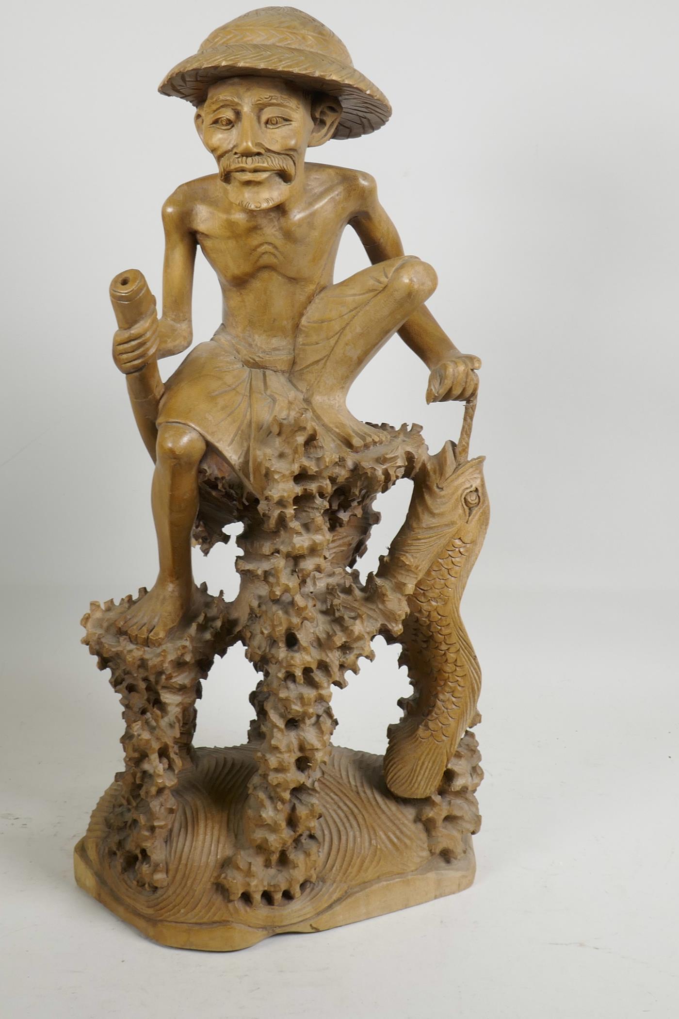 An oriental carved wood figure of a fisherman with large fish, seated on a coral reef, 21" high, A/F