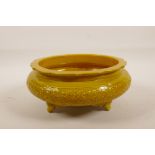 A Chinese yellow ground porcelain censer on tripod supports with a lobed rim and raised scrolling