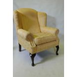A Georgian style wing back armchair, raised on cabriole supports