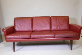 A mid century red leather three seat sofa raised on turned supports, 71" wide x 21" high