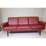 A mid century red leather three seat sofa raised on turned supports, 71" wide x 21" high