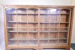 An early C20th large pine open bookcase with glazed sliding doors and bracket feet, 85" x 14", 58"