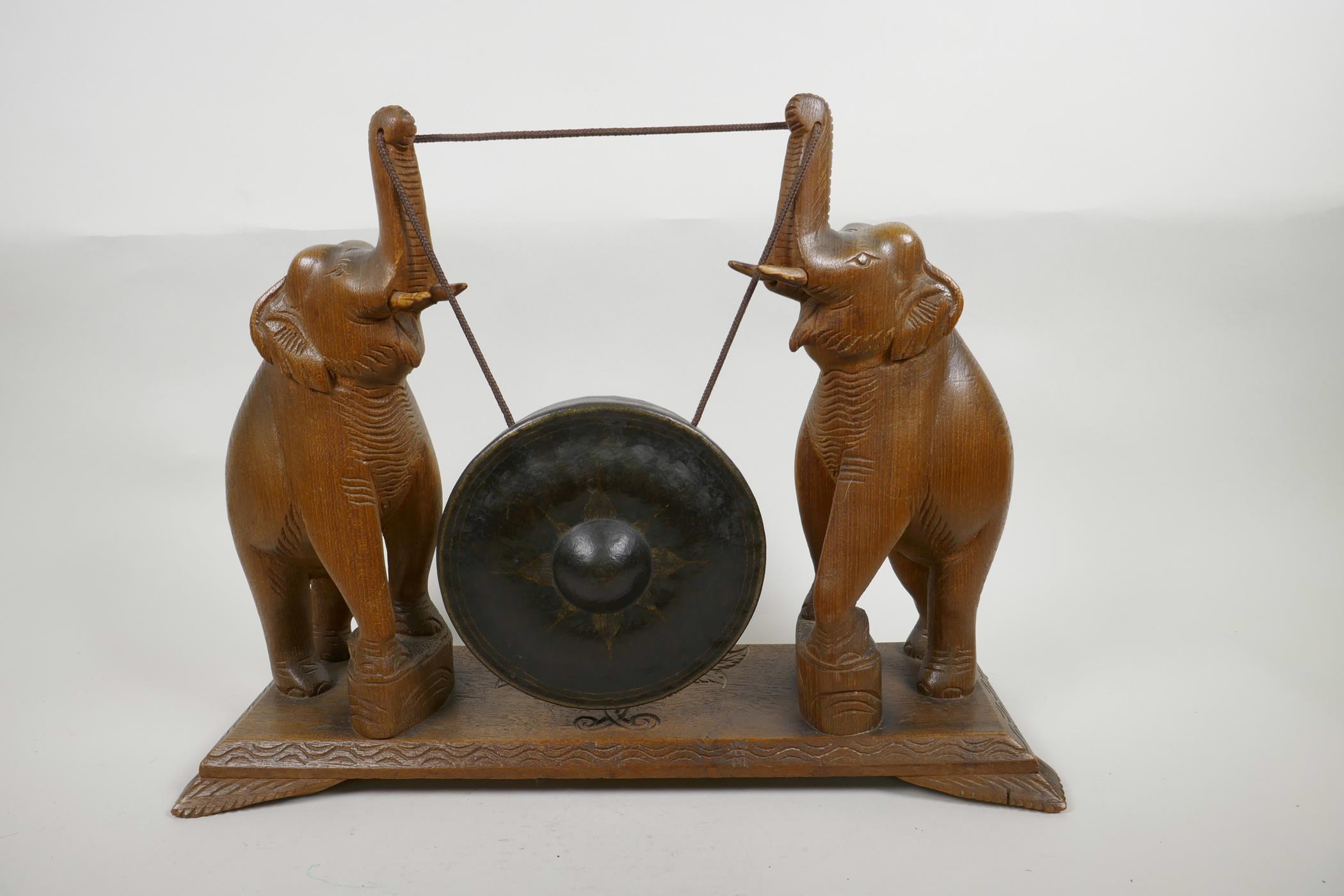 A bronze dinner gong, the wooden stand carved as two elephants with raised trunks, 13" high, 17"