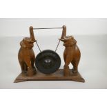 A bronze dinner gong, the wooden stand carved as two elephants with raised trunks, 13" high, 17"