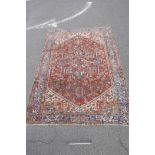 An old Persian Heriz carpet decorated with a geometric pattern on a red field with blue borders,