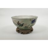 A Chinese crackleware bowl with famille verte decoration of birds in a landscape, on a carved