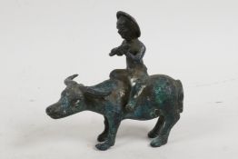 A small Chinese bronze figurine of a boy playing the flute whilst sitting on the back of a