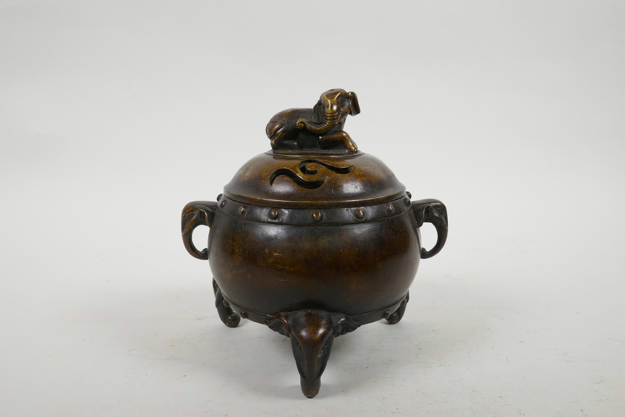 A Chinese bronze barrel shaped censer with two elephant mask handles and elephant knop, raised on