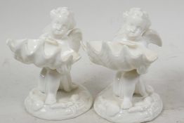 A pair of Royal Worcester white glazed porcelain table salts modelled as cherubs holding large