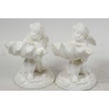 A pair of Royal Worcester white glazed porcelain table salts modelled as cherubs holding large