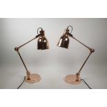 A pair of rose gold coloured contemporary Anglepoise style desk lamps