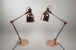 A pair of rose gold coloured contemporary Anglepoise style desk lamps