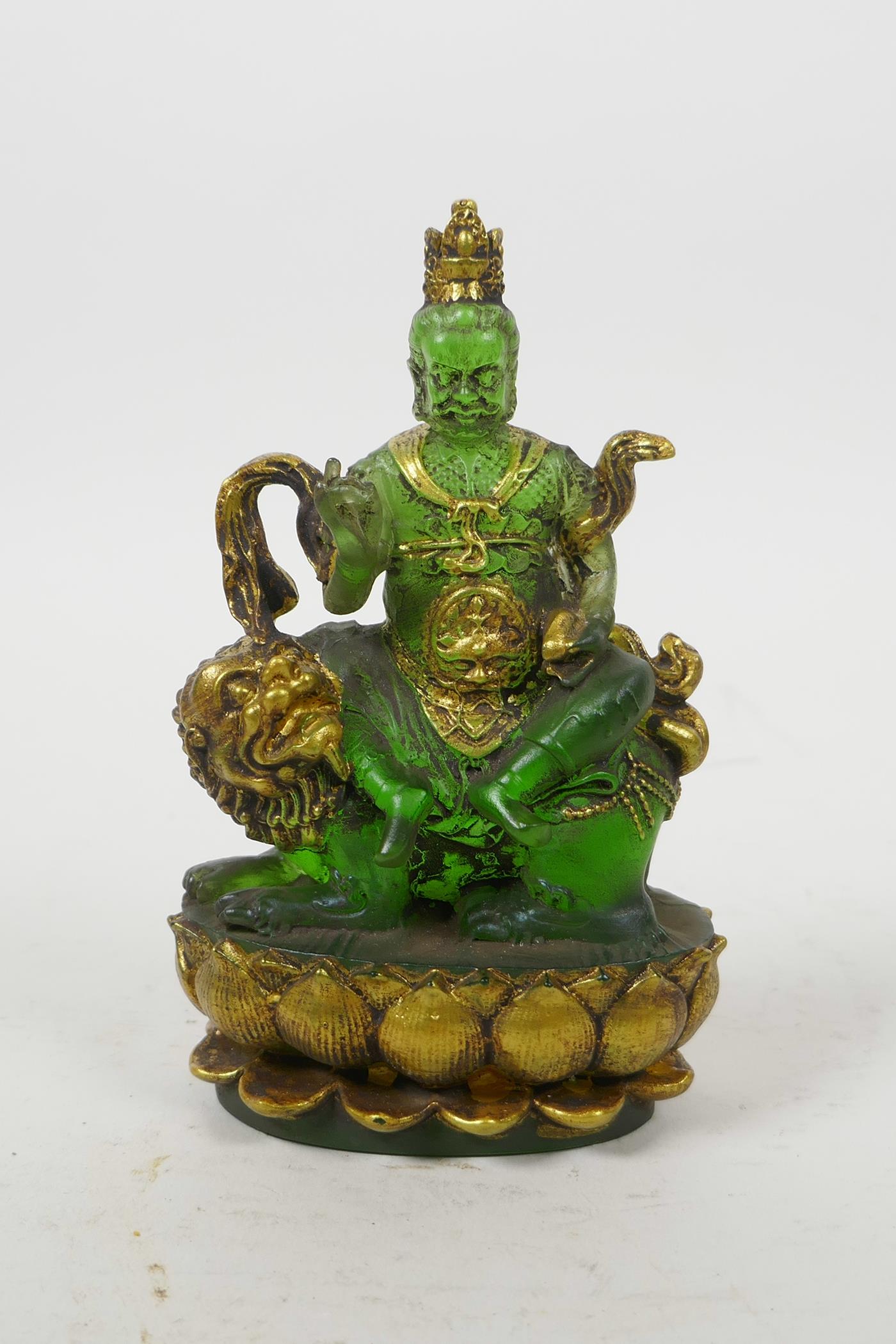 A Tibetan pressed green glass figure of a wrathful deity sitting on a temple lion, 5" high