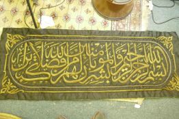 A large Islamic wall hanging having stumpwork decoration of scripture in gold thread, 56" x 23"