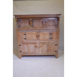 A limed oak court cupboard, with carved frieze and door panels, with iron hinges and raised on stile