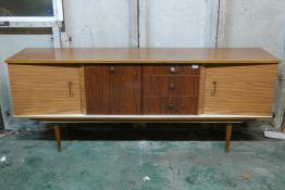 A mid century formica sideboard, with inverted front of two cupboards flanking a fall and three