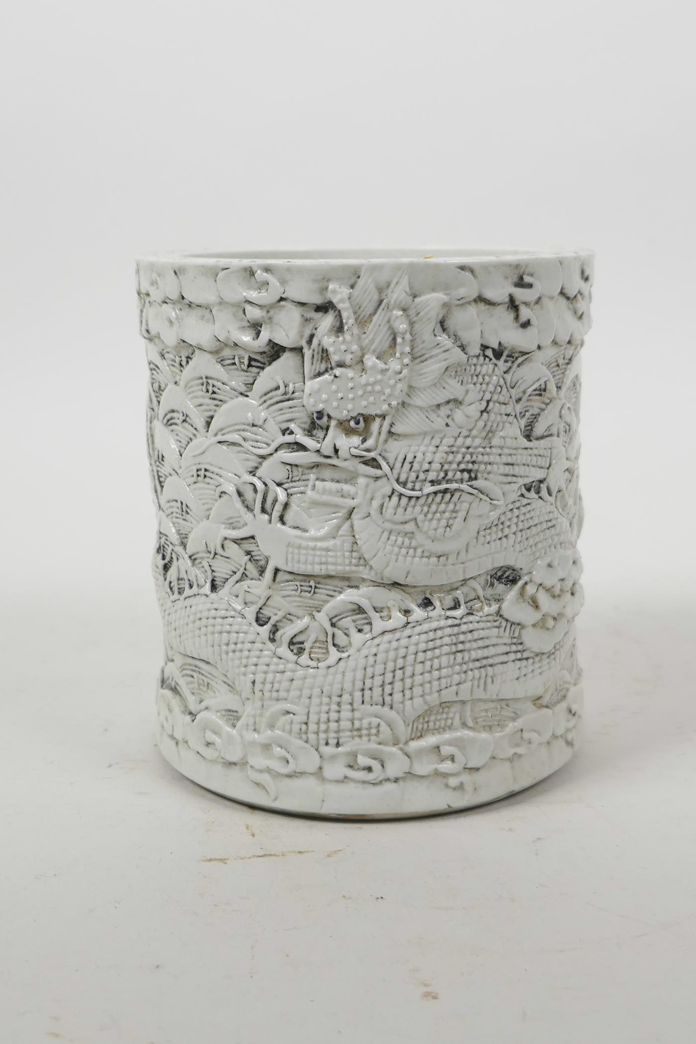 A Chinese moulded porcelain brush pot with raised decoration of dragons above water, impressed