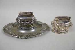 A silver plated table lighter on embossed companion ashtray, together with a similar lighter