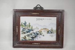 A Chinese famille verte porcelain panel depicting a riverside landscape, mounted in a hardwood