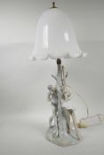 A Lladro porcelain table lamp in the form of two ballet dancers around a tree with milk glass shade,