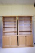 A pair of contemporary light oak veneered open bookcases with two cupboards below, in two