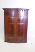 A Georgian flame mahogany bowfront hanging corner cupboard with two doors over a single drawer,