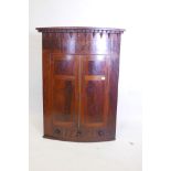 A Georgian flame mahogany bowfront hanging corner cupboard with two doors over a single drawer,