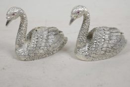 A pair of silver plated salt and peppers cast in the form of swans with red stone set eyes, 2" long